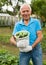 Happy elderly man farmer with bucket of cucumbers in the garden