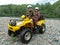 Happy elderly man and woman in camouflage suits and motorcycle helmets ride a yellow ATV. Sports, recreation