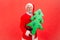 Happy elderly santa claus with gray beard in eyeglasses holding paper decorated christmas tree, preparing for winter holidays
