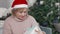 Happy elderly woman in Santa Claus hat holding out a gift to the camera