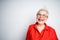 Happy elderly woman in shirt and glasses laughs opening mouth and squirts on gray background
