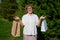 A happy elderly woman is standing in a park and holding paper bags. A retired shopaholic enjoys shopping. The concept of