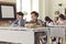 Happy elementary school boys listening to teacher sitting at desk in modern classroom