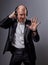 Happy emotional dancing and singing bald man listening the music in wireless headphone on dark grey background and showing five