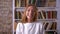 Happy enjoyable laughing caucasian female standing next to camera, books on background, casual style