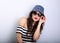 Happy enjoyment grimacing young woman in sunglasses and blue baseball cap posing and looking in striped blouse on blue empty