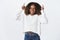 Happy enthusiastic and carefree attractive young african-american woman with curly hair in winter white trendy sweater