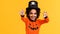 Happy ethnic boy in pumpkin costume scary make gestures and celebrates Halloween and laughs on yellow background