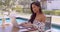 Happy ethnic young woman using laptop near swimming pool