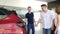 A happy European couple is talking to a car dealer at a dealership, discussing cars, considering a luxury new model