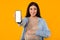 Happy european pregnant lady with big belly showing smartphone with white blank screen on yellow background, mockup