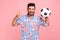 Happy excited bearded man with dark hair and beard wearing blue shirt posing with soccer ball and