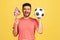 Happy excited bearded man in striped t-shirt smiling holding in hands flag of United Kingdom and football ball, supporting