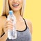 Happy excited cheerful smiling woman in sportswear, bottle of water. Yellow background. Fitness instructor, trainer coach. Girl