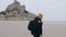 Happy excited European tourist man with backpack walking away from epic Mont Saint Michel castle in Normandy slow motion