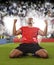 Happy and excited football player in red jersey celebrating scoring goal kneeling on grass pitch