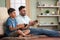 Happy excited indian father with son playing video game using joystick on floor at home - concept of Joyful playtime
