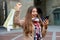 Happy excited shopper woman laughs watching phone raised arm with shopping bag outdoor in city street