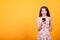 Happy exited pretty girl in short dress holding mobile phone in studio over yellow background