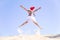 Happy expressive little girl wearing a red Santa hat jumping and enjoying life on the sandy beach by the sea on clear sunny day