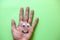 Happy face made with plastic eyes and drawn smile on a human hand palm, with green background.