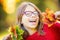 Happy fall girl smiling and joyful holding autumn leaves. Beautiful young girl with maple leaves in red cardigan