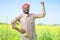 Happy famer showing stroing gesture while standing at farmland by looking at camera - conept of confident, agro business