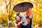 Happy family is in autumn city park. Peoples are posing under umbrella. Children and parents are smiling, playing and having fun.
