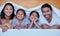 Happy family in bed. Portrait of hispanic family in bed. Young family under a bed sheet. Two parents bonding with their