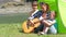 A happy family camping at the river, playing the guitar and singing a song together in the tent.