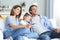 Happy family with child sitting on sofa watching tv, young parents embracing daughter relaxing on couch together