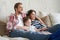 Happy family with child sitting on sofa watching tv, young parents embracing daughter relaxing on couch together.