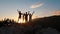 Happy family with children raising hands while standing in mountains at sunset