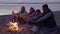 Happy family with children warm hands by fire on beach