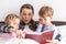 happy family. Close up loving mother lying with daughter son two kids pajamas in bed children reading interesting