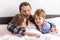 happy family. Close up loving mother lying with daughter son two kids pajamas in bed children reading interesting