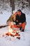Happy family couple in love basking by camp fire outside in winter snowy forest