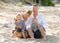 Happy family couple sitting on beach sand with baby boy son and daughter