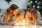 Happy family with daughter lies on the floor and cozy talks by the light of garlands against the background of Christmas tree.