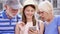 Happy family enjoying vacation. Seniors and their daughter standing on street browsing in smartphone