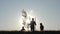 A happy family of farmers. Silhouette of a father and two children planting and watering a tree in the Park at sunset.