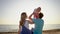 Happy family - father, mother and baby sitting on the sunset sea beach. Parents with children on summer vacations