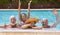 Happy family of four senior people floating in outdoor swimming pool raising splashes of water. They smile relaxed on vacation