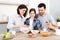 Happy family have healthy breakfast together. Smiling mother pours milk in bowl with cornflakes, eat apples, snacks and