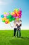 Happy family holding colorful balloons. Mom, ded and two daughters playing on a green meadow.