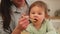 Happy family at home. Mother feeding her baby girl from spoon in kitchen. Little toddler child with messy funny face