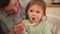 Happy family at home. Mother feeding her baby girl from spoon in kitchen. Little toddler child with messy funny face