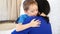 Happy family: joyful child hugging his mom on a white sofa at home