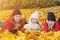 happy family lies on yellow maple leaves in sunny park. mother with kids enjoying fall weather outdoors
