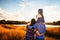 Happy family with a little daughter in a field in nature, looking forward, view from the back, in the rays of the sunset